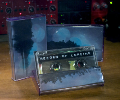 an alternate angle of three cassettes on a desk with blurred out audio gear in the background